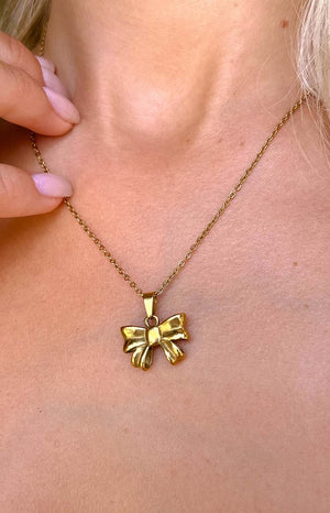 blonde girl wearing a gold bow necklace with baby pink nails