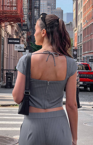 Girl walking away in grey striped top with sunglasses on her head holding a black mini bag