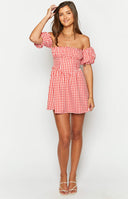 Brunette girl wearing red checkered mini dress holding wine glass in front of table.