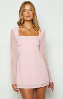 Light pink wrap style mini dress with gathered bust and sheer long sleeves styled on brunette model.