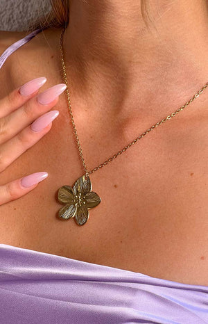 girl wearing a gold necklace with frangipani pendant, purple tank top with pink finger nails