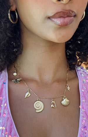 Girl wearing oink sequin dress and gold sea shell necklace.