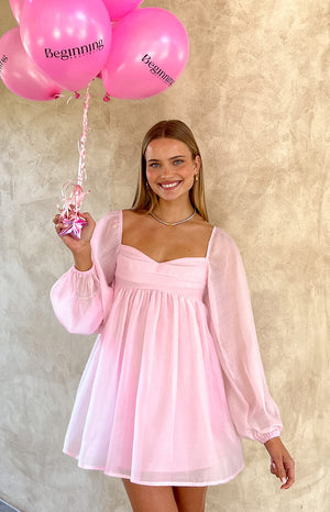 Model holding pink balloons wearing a long sleeve pink mini dress.