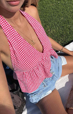 girl wearing red gingham halter crop top paired with light wash denim shorts