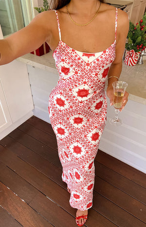 Model wearing red and white print maxi dress and red heels holding wine glass.