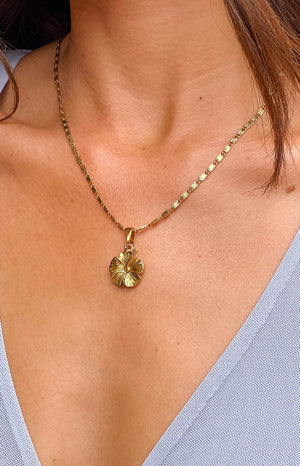 Brunette girl wearing a gold flower necklace and blue lilac dress.