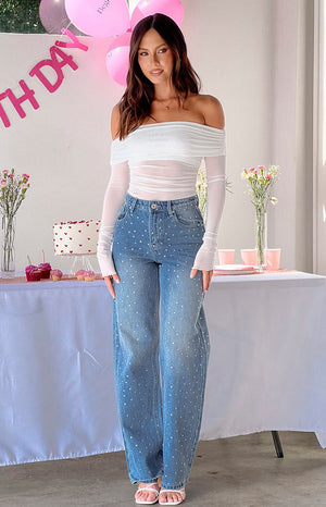 Girl wearing sparkle denim jeans and white off the shoulder top in front of birthday table.