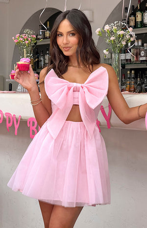 Brunette model wearing pink bow mini dress holding a pink cupcake.