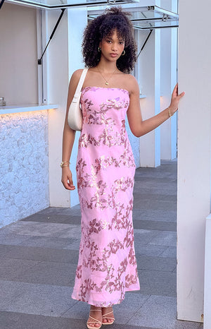 Girl wearing pink maxi dress and nude heels with a matching bag in outdoor area.