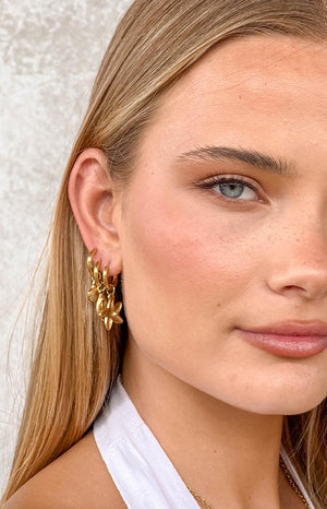 a blonde model wears three gold earrings with sea-themed pendants and a white top