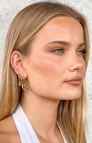 a girl with blonde hair wears three gold pendant earrings 