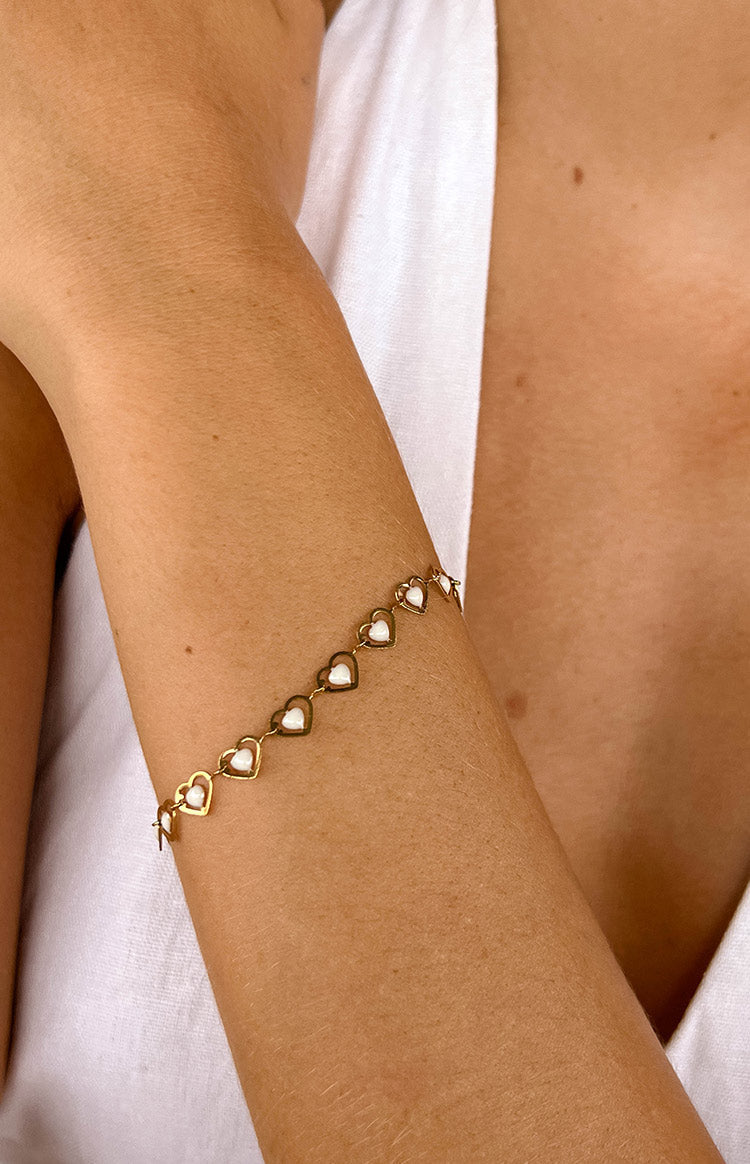 a girl wears a gold heart bracelet with white peals in the middle