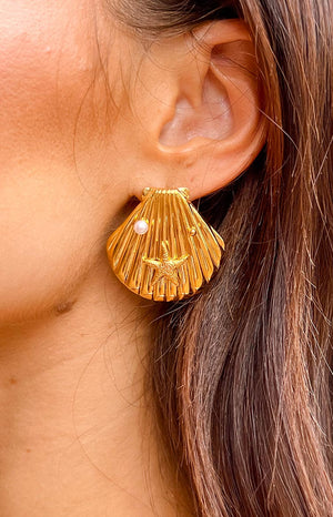 Brunette girl wearing gold seashell earrings with a starfish and pearl.