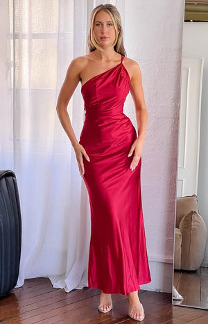 blonde model wearing a red satin one shoulder maxi dress paired with clear heels and delicate gold jewellery