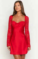 a blonde girl wears a red lace mini dress with long sleeves beside a table with red roses and candles