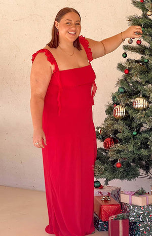 Brunette model wearing a red maxi dress with ruffle straps and red cherry earrings at Christmas.