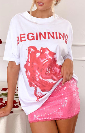 a white printed t-shirt with a pink rose and the word 'beginning' and a pink sequin mini skirt is worn by a blonde model