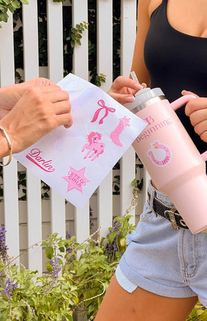 girl holding sticker sheet with assorted pink designs and sticking them onto a pink metal water bottle