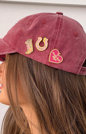 brunette girl wearing a red baseball cap with three western style pins - a cowboy boot with a bow