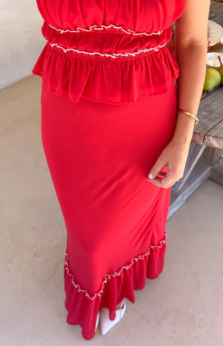 Girl wearing a red two piece top and maxi skirt set with white ruffle details styled with a gold bracelet and white point toe heels.