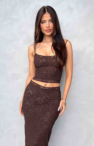 Brunette girl wearing a brown lace tank top and matching maxi skirt standing in front of a wall.