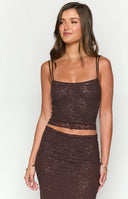 Brunette girl wearing a brown lace tank top and matching maxi skirt standing in front of a wall.