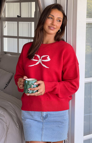 Brunette girl wearing red bow sweater and denim mini skirt holding christmas mug.