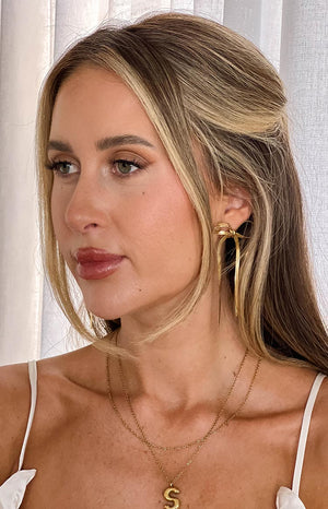 blonde model wearing gold bow dangle earrings and a gold necklace stack