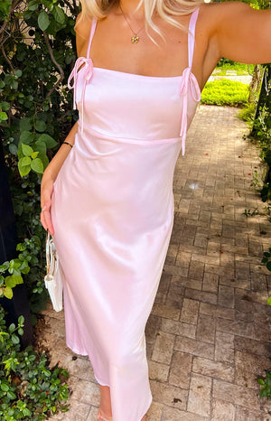 model wearing a baby pink maxi dress with bows at straps and a gold pendant necklace holding a white purse