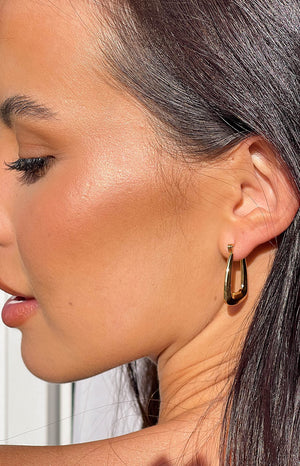 Side profile of brunette girl wearing gold square hoop earrings.