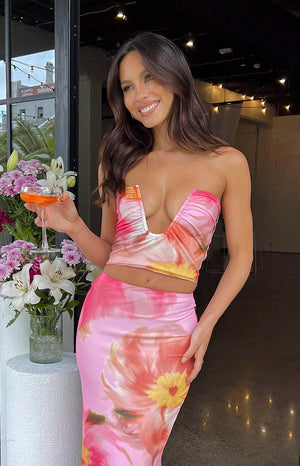 Brunette model wearing pink floral strapless top and skirt holding a drink.