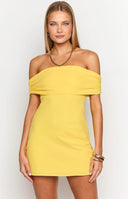 Brunette model wearing yellow off the shoulder dress holding a tan handbag.