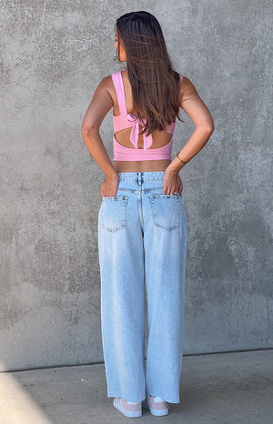 Back of a brunette girl in blue denim jeans and a pink top, with her hands in her pockets.