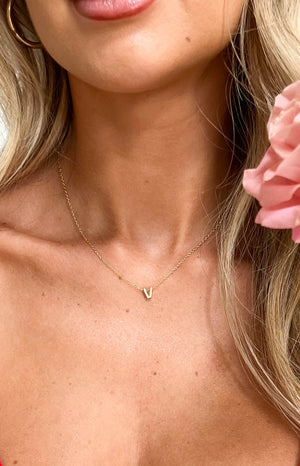 close up image of model wearing letter V gold necklace