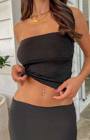 Zoomed in photo of brunette model excluding face wearing a chunky gold necklace and black body-con tube top with a matching black midi skirt